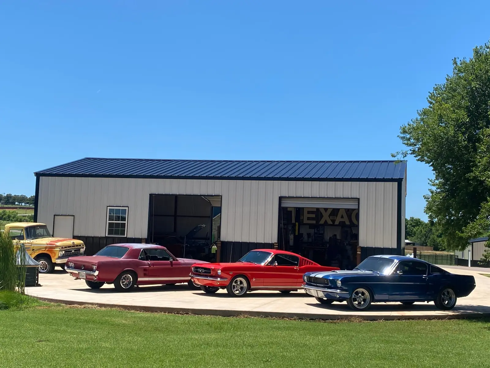Three classic Mustangs and a flame-painted vintage Ford pickup lined up in front of the Red Dirt Classics shop